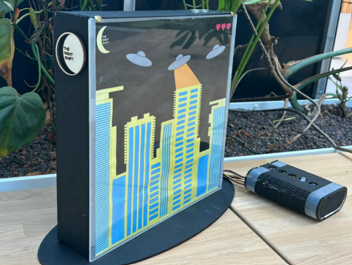 NightShift physical prototype, a lit cityscape artwork with a remote control